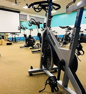 A gym room with several stationary bikes and a large white screen on the wall.