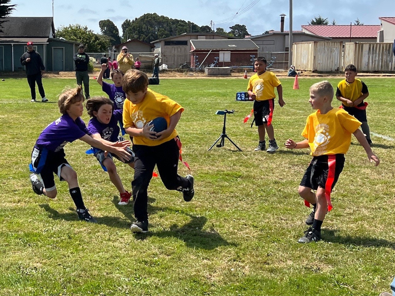 Children playing flag football outdoors on a sunny day.