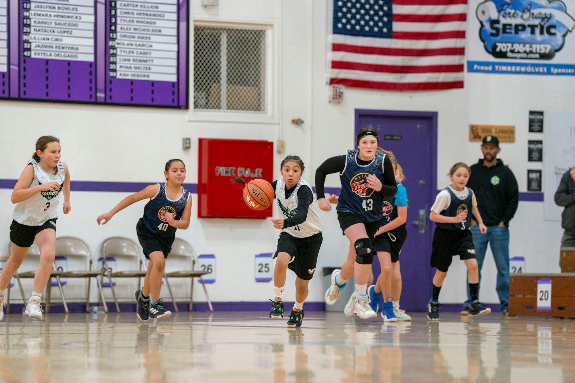 A group of kids playing basketball indoors, one dribbling the ball.