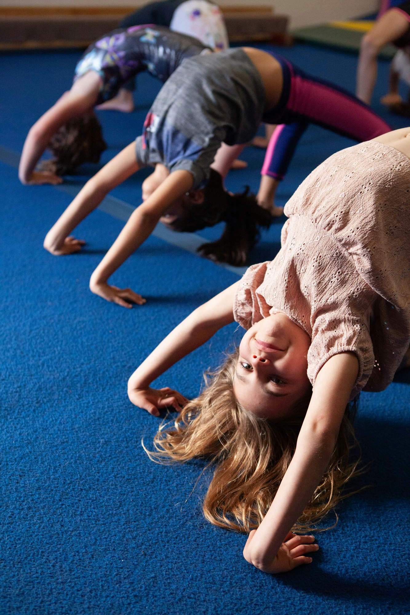 Children practicing yoga or gymnastics in a forward bend pose on a blue floor mat.