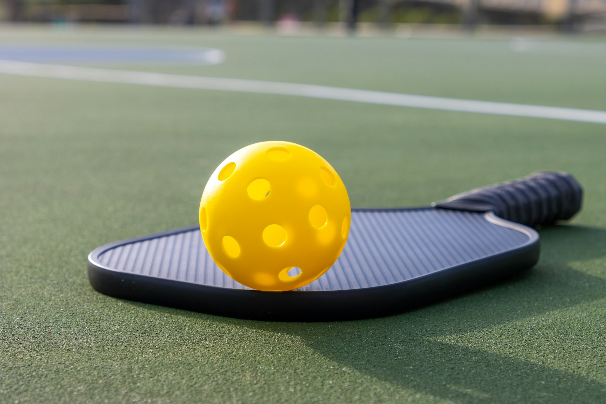 Yellow pickleball and paddle on a green court surface.