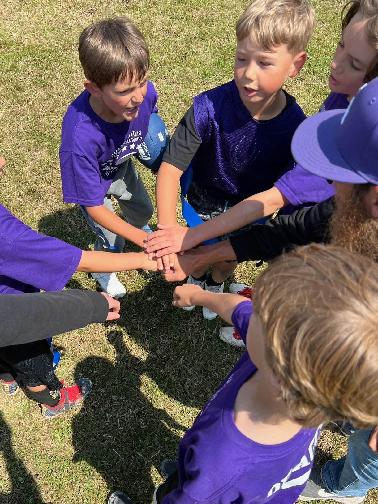 Group of children in purple shirts doing a team hand stack outdoors.