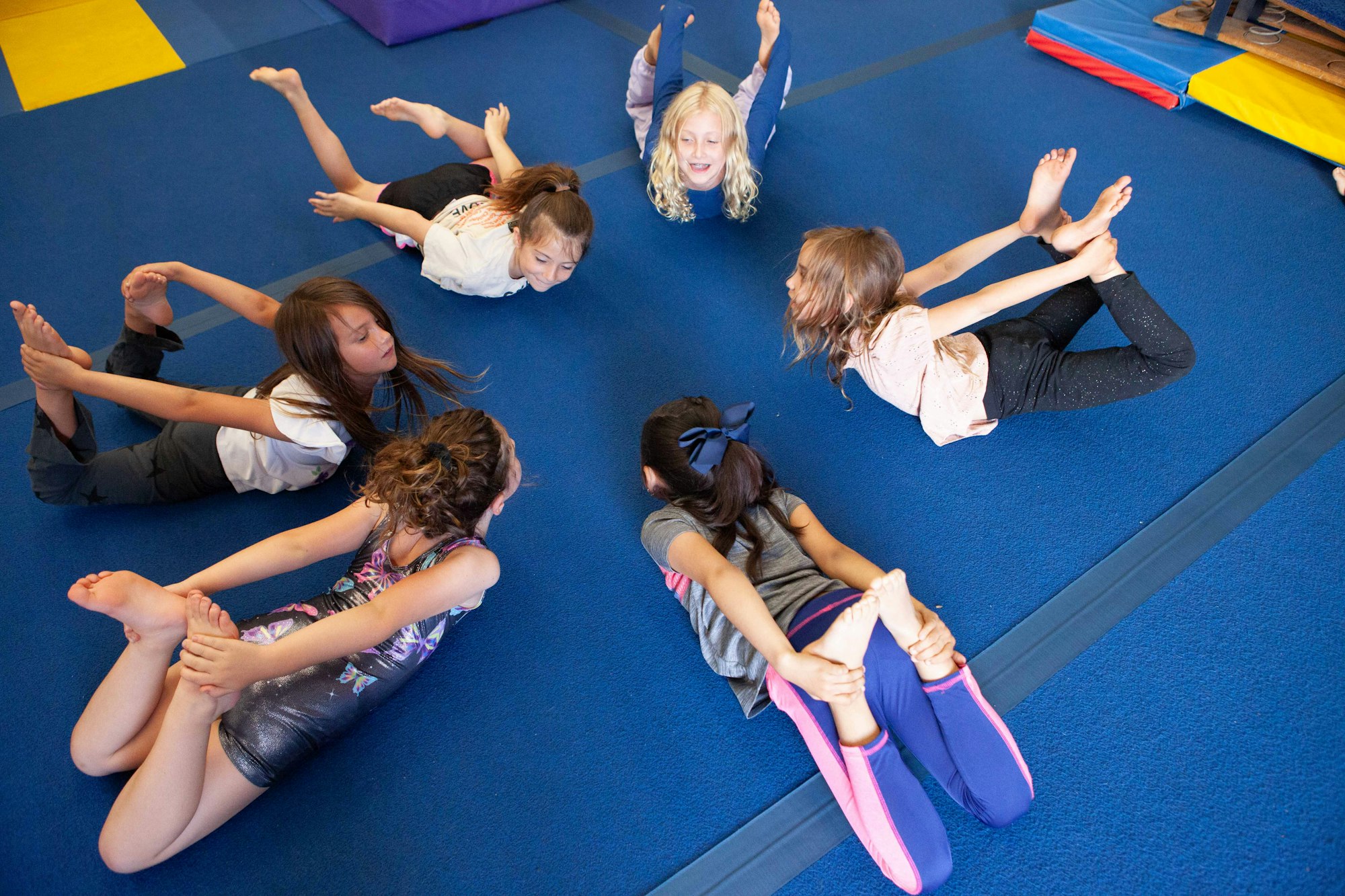Children practicing a yoga pose in a circle on a blue mat.