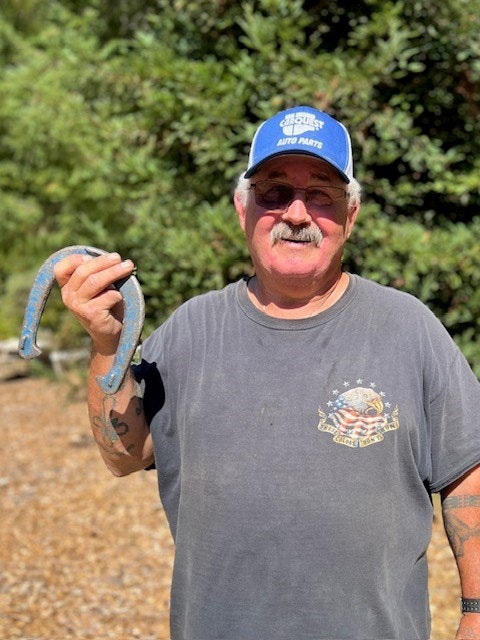 Man with a cap holding a blue object, smiling outdoors.