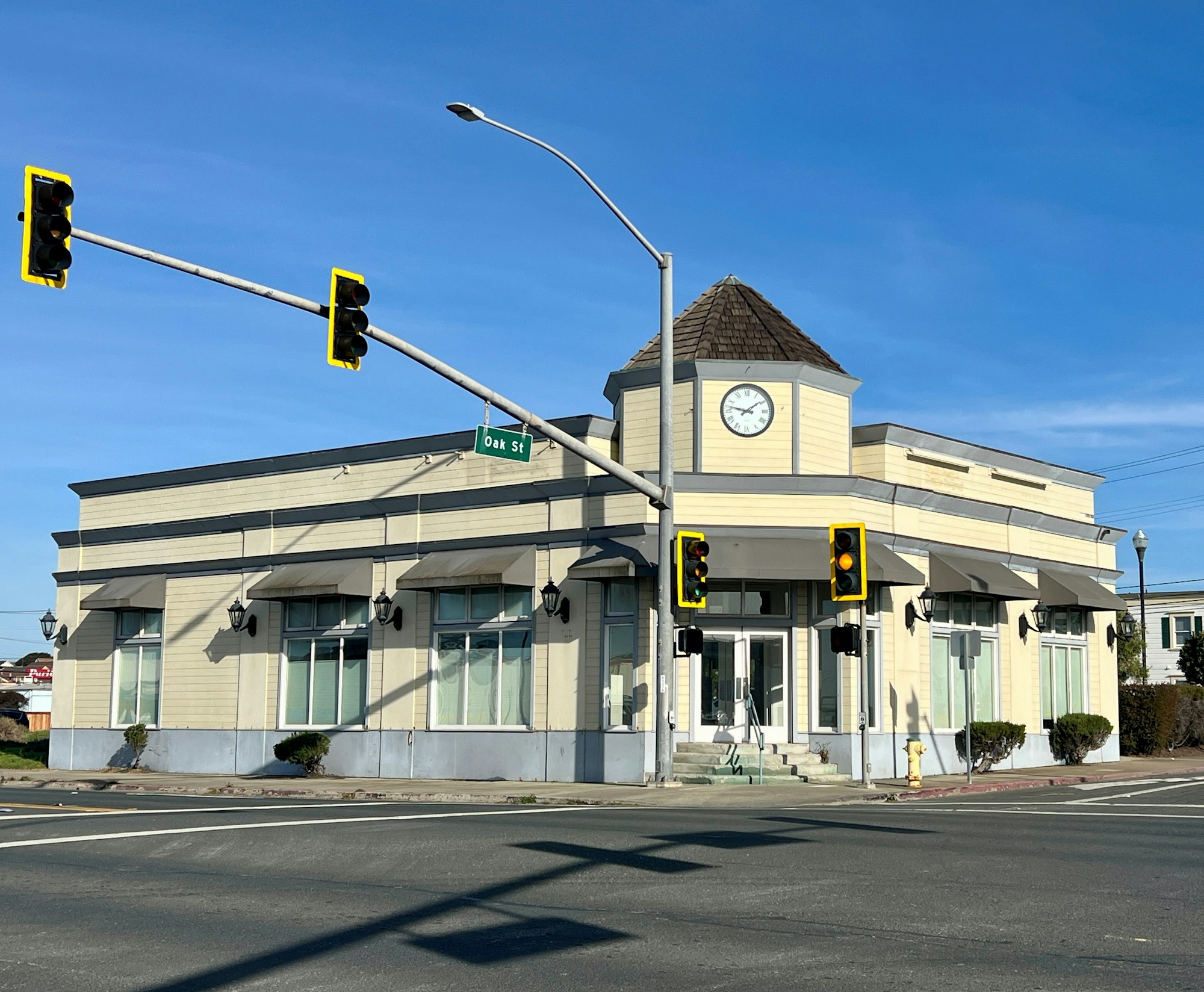 A building with a clock tower at a street corner, traffic lights, and Oak St sign.