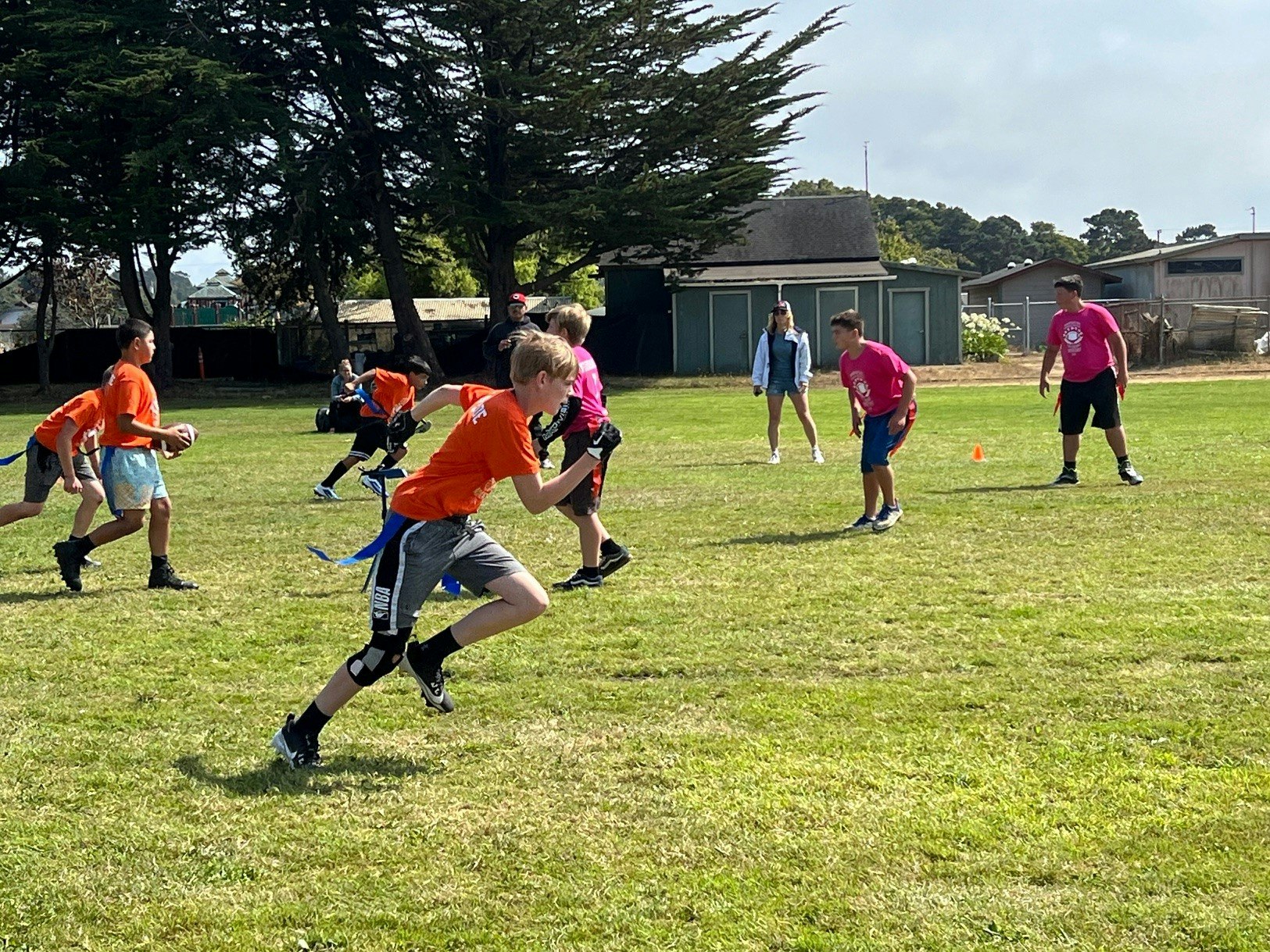 Kids playing flag football on a sunny field.