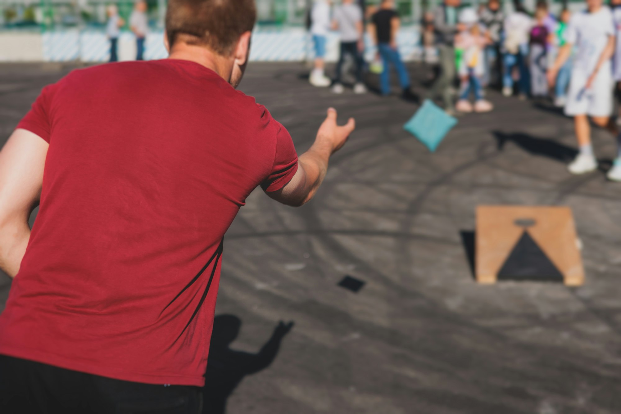 Person in red shirt playing cornhole, throwing a beanbag towards a board.