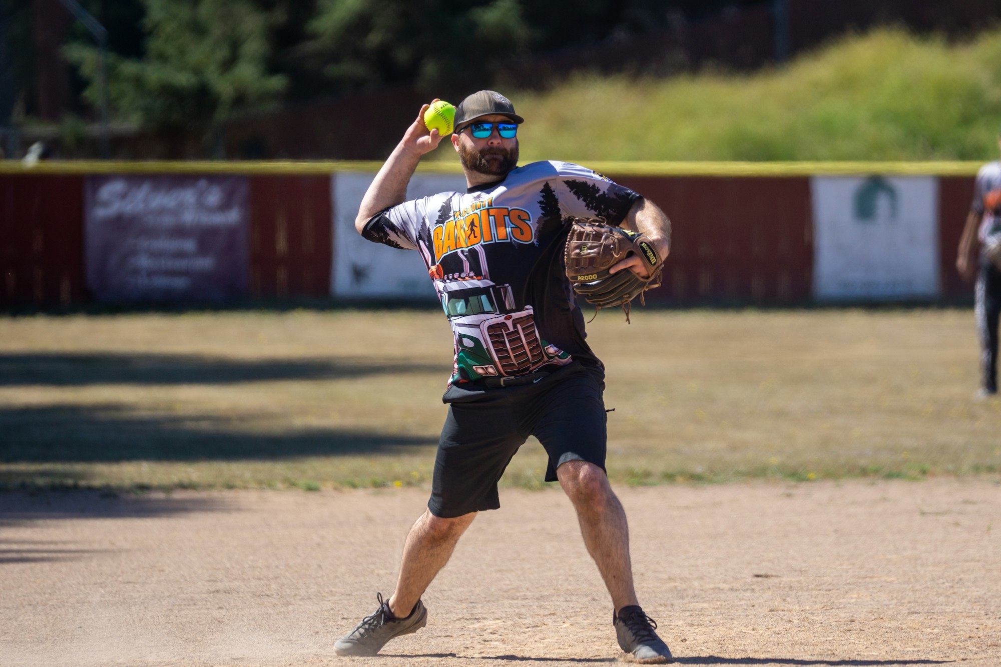 A man playing softball, preparing to throw a ball, wearing a "Bandits" shirt.