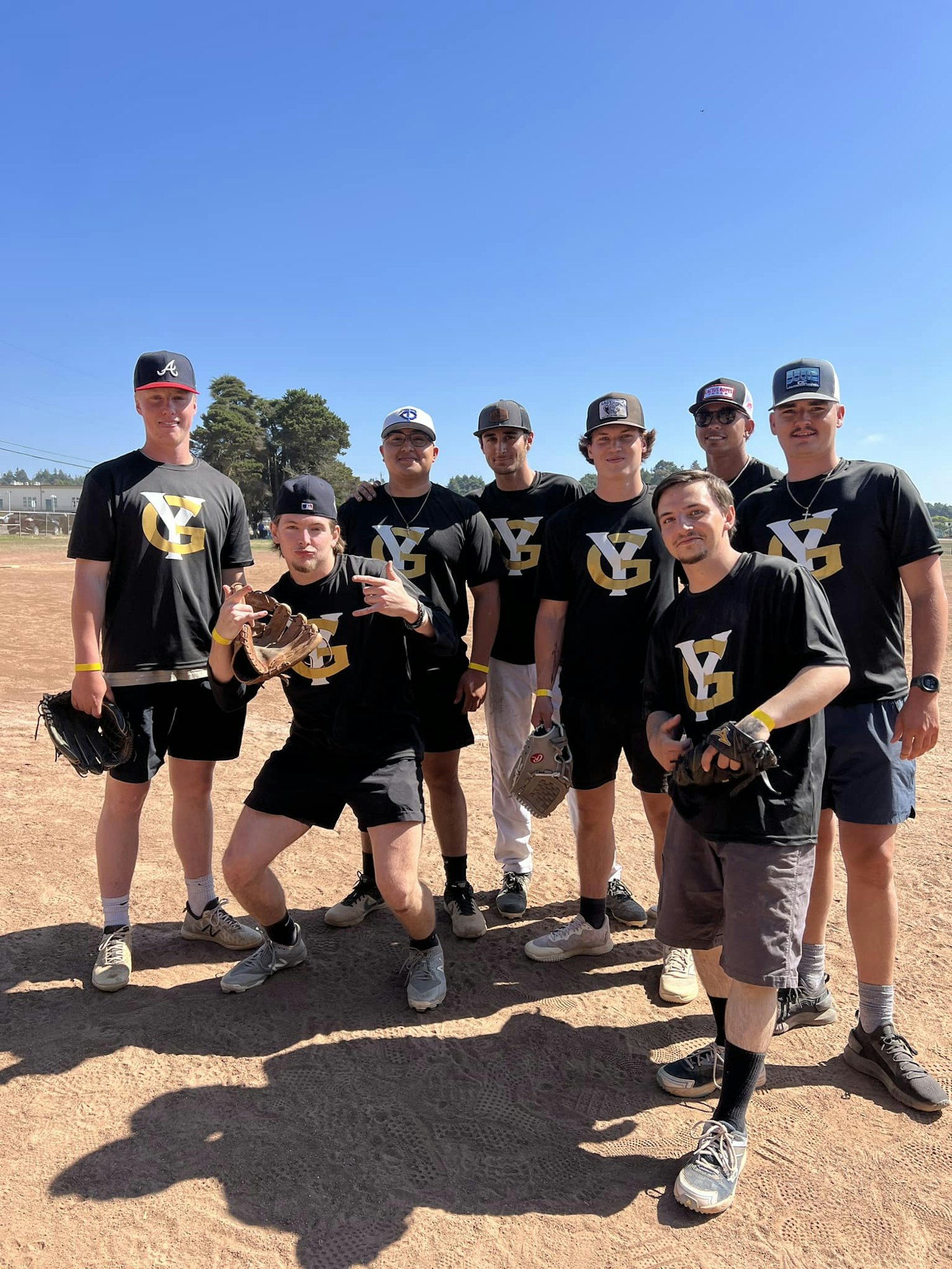 A group of individuals in matching black and gold T-shirts and baseball caps on a field.