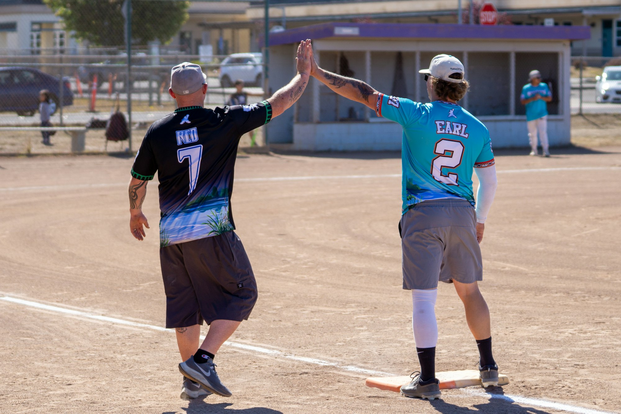 Two baseball players on a field high-five near a base, wearing jerseys with names and numbers.