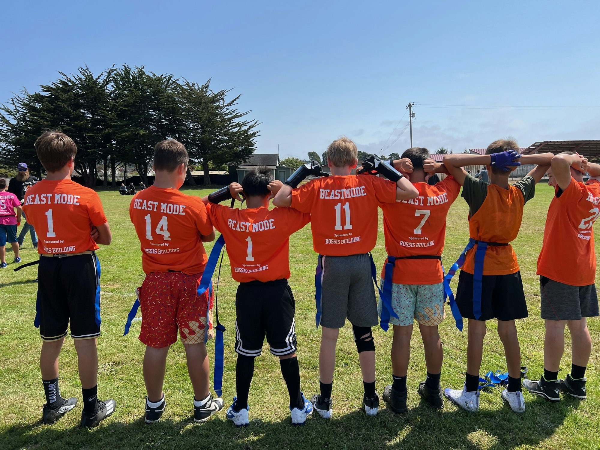 Kids in orange "BEAST MODE" shirts with linked arms on a sunny field.