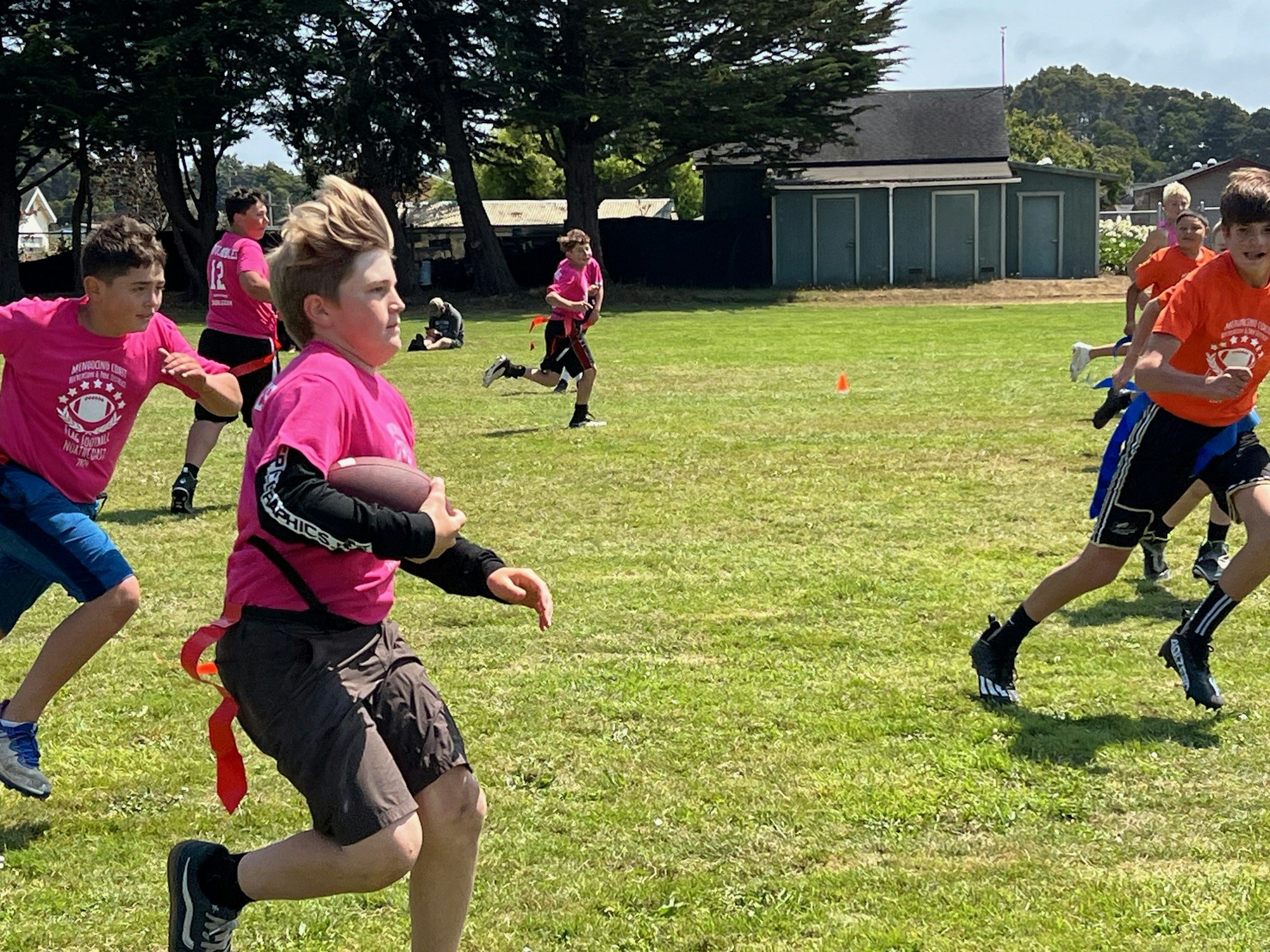 Young players in colorful shirts engaged in a flag football game on a grassy field.
