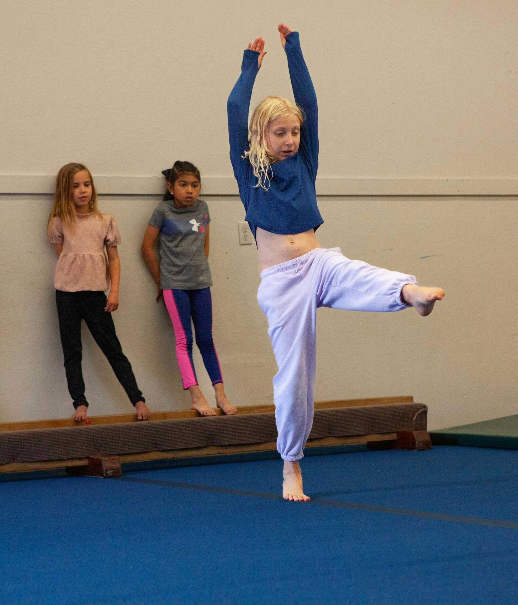 A child practicing martial arts with others watching in a gym.
