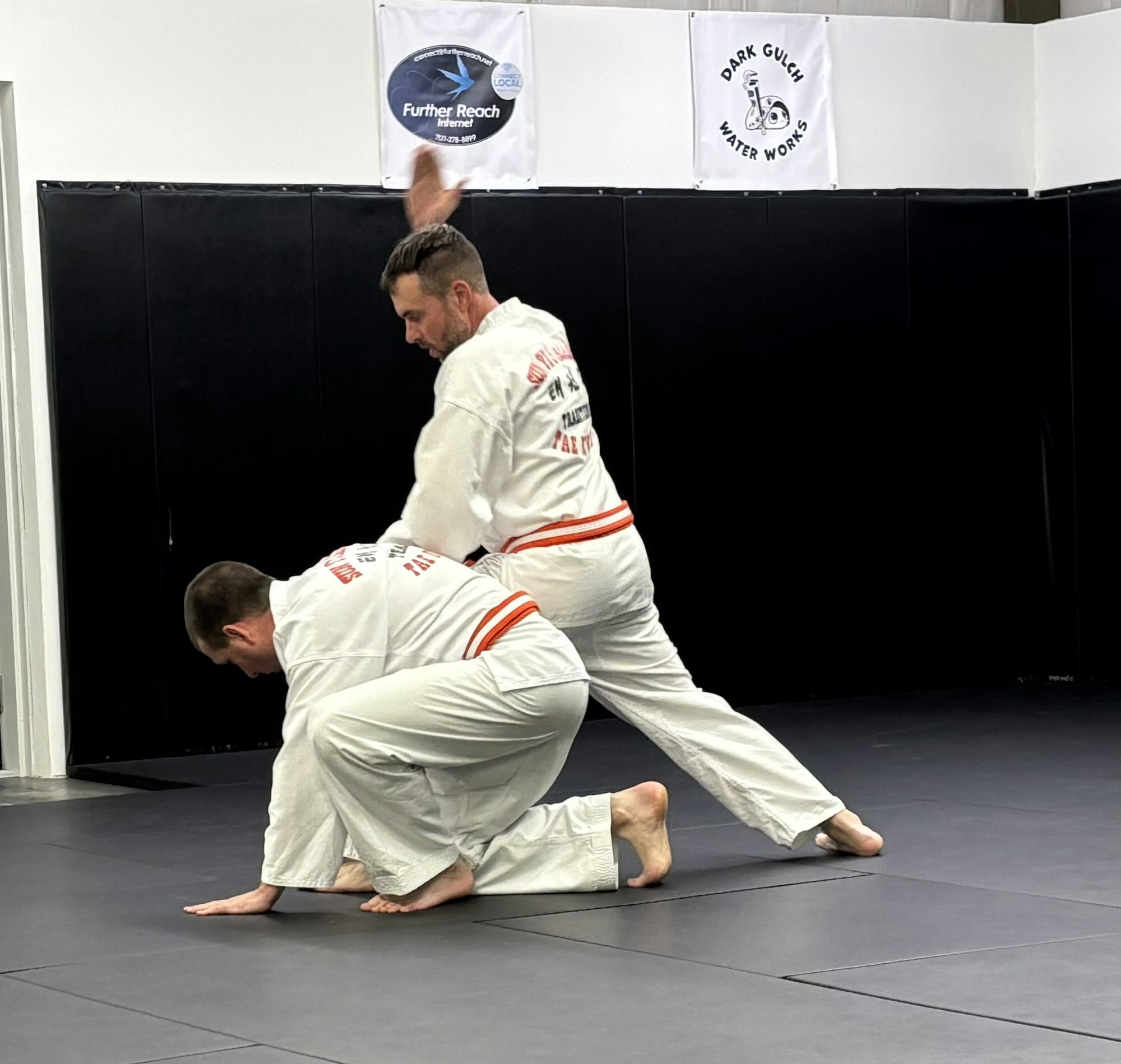 Two people in martial arts uniforms practicing in a dojo.