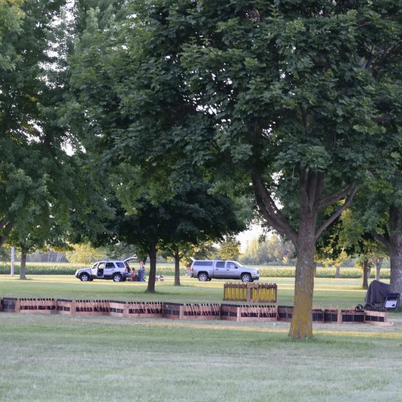 The image shows two parked trucks among trees, with wooden boxes likely containing fireworks set up in a grassy area.