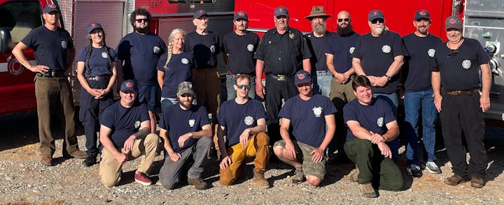 A group of firefighters in uniforms poses for a photo in front of a fire truck.