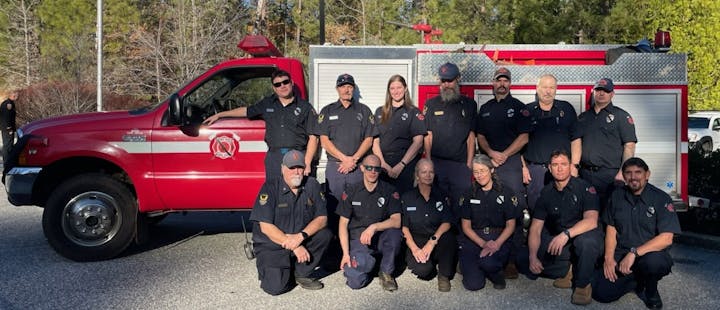 A group of firefighters in uniform posing in front of a red fire truck.