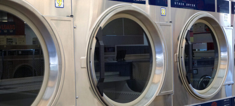 Three stainless steel stack dryers in a laundromat.