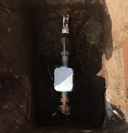 A water meter installed in the ground with exposed piping.