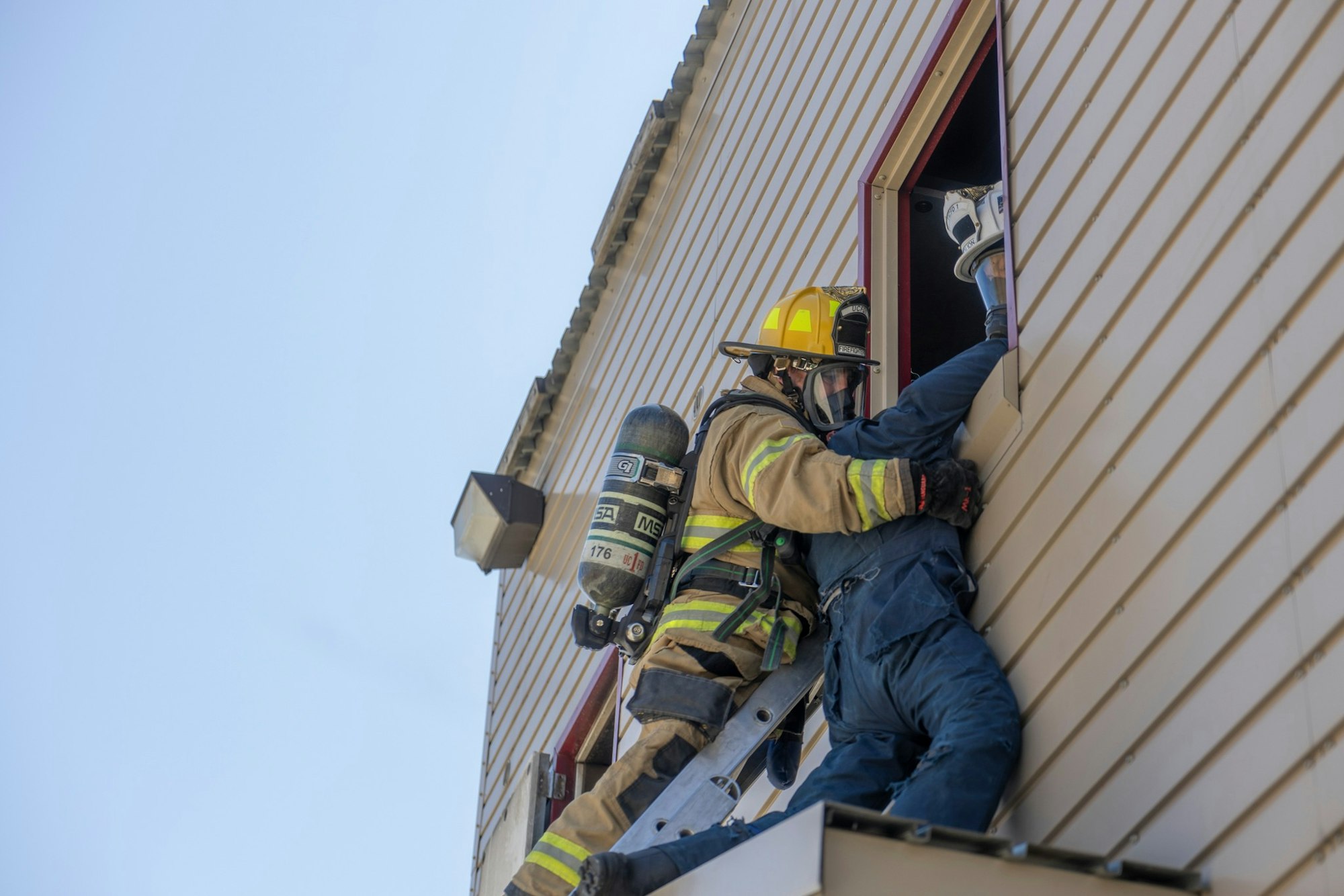 A firefighter on a ladder rescuing a person through a window of a building.