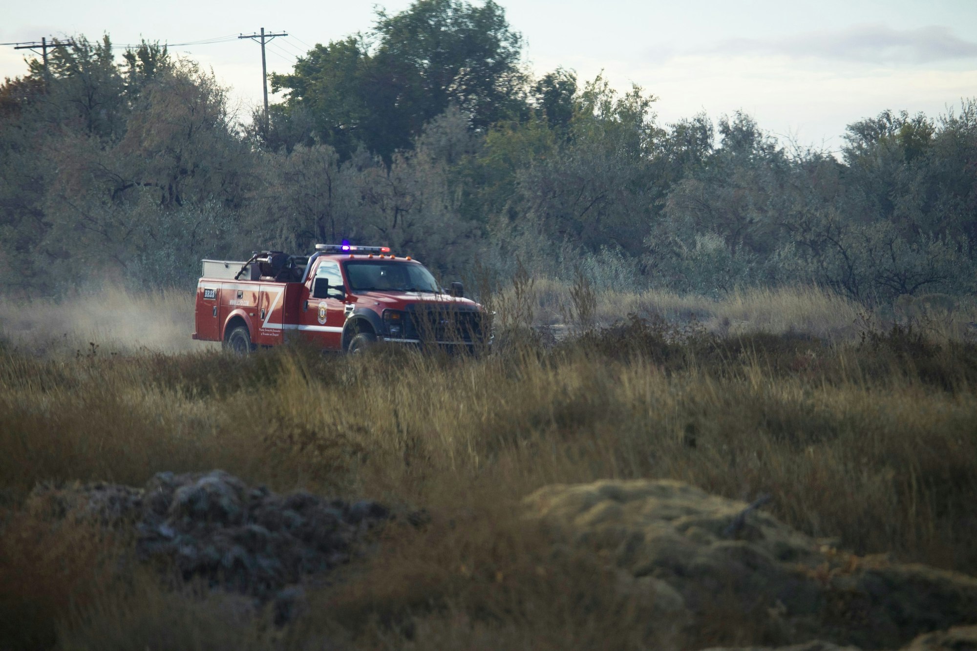 A red fire truck driving on a grassy dirt road with trees in the background.