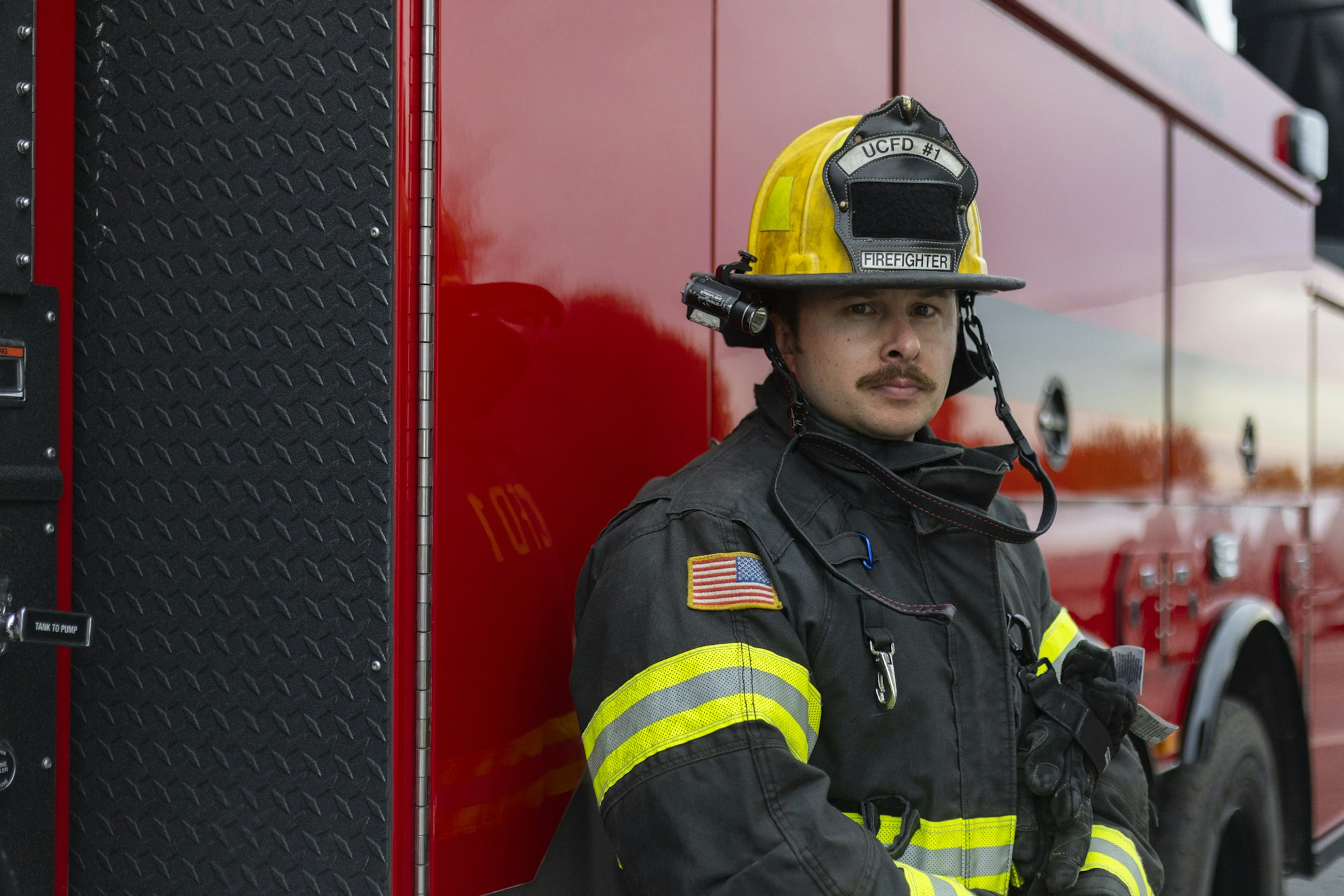 A firefighter in uniform stands beside a red fire truck.