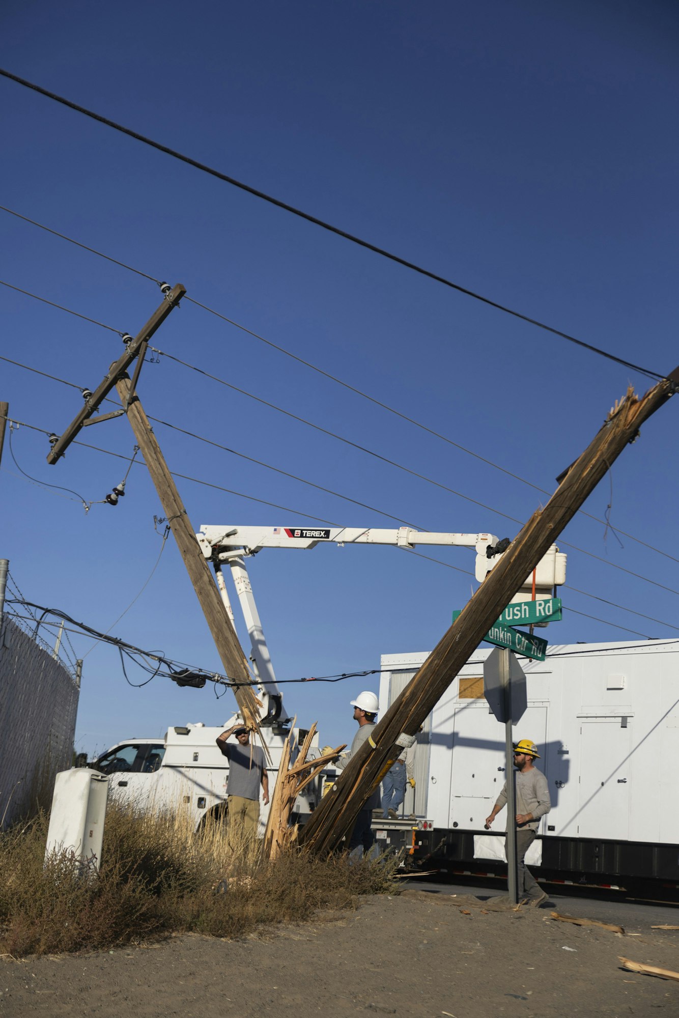 Workers repair broken utility poles using a bucket truck at an intersection.