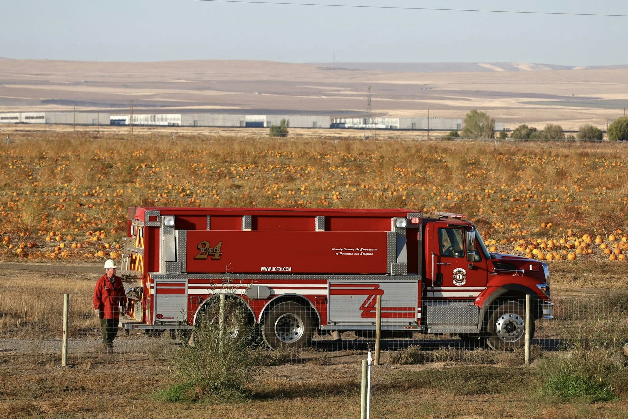 A fire truck beside a pumpkin field with a person in a hard hat and red shirt walking nearby.