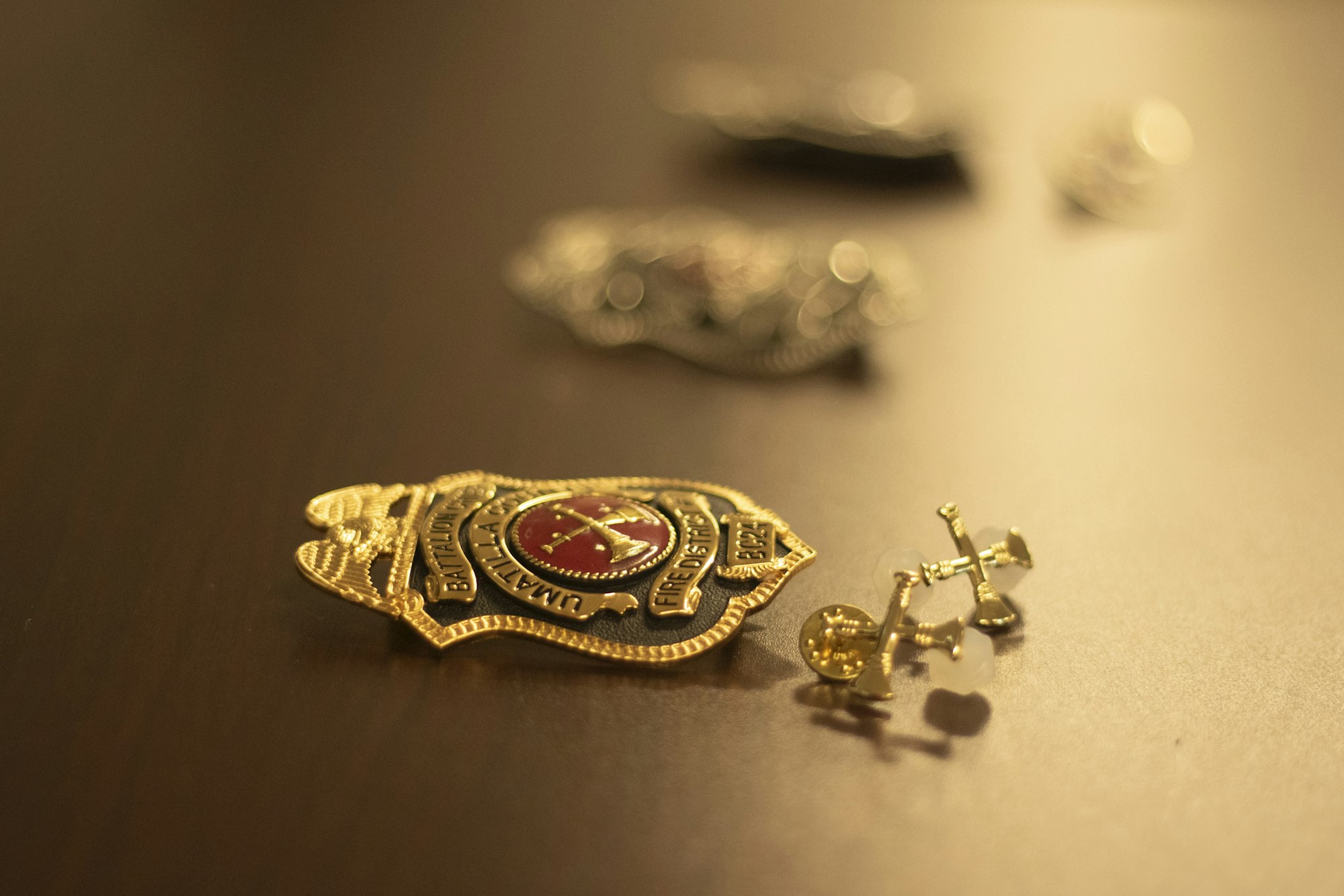A close-up of a gold badge and small pins on a wooden surface.