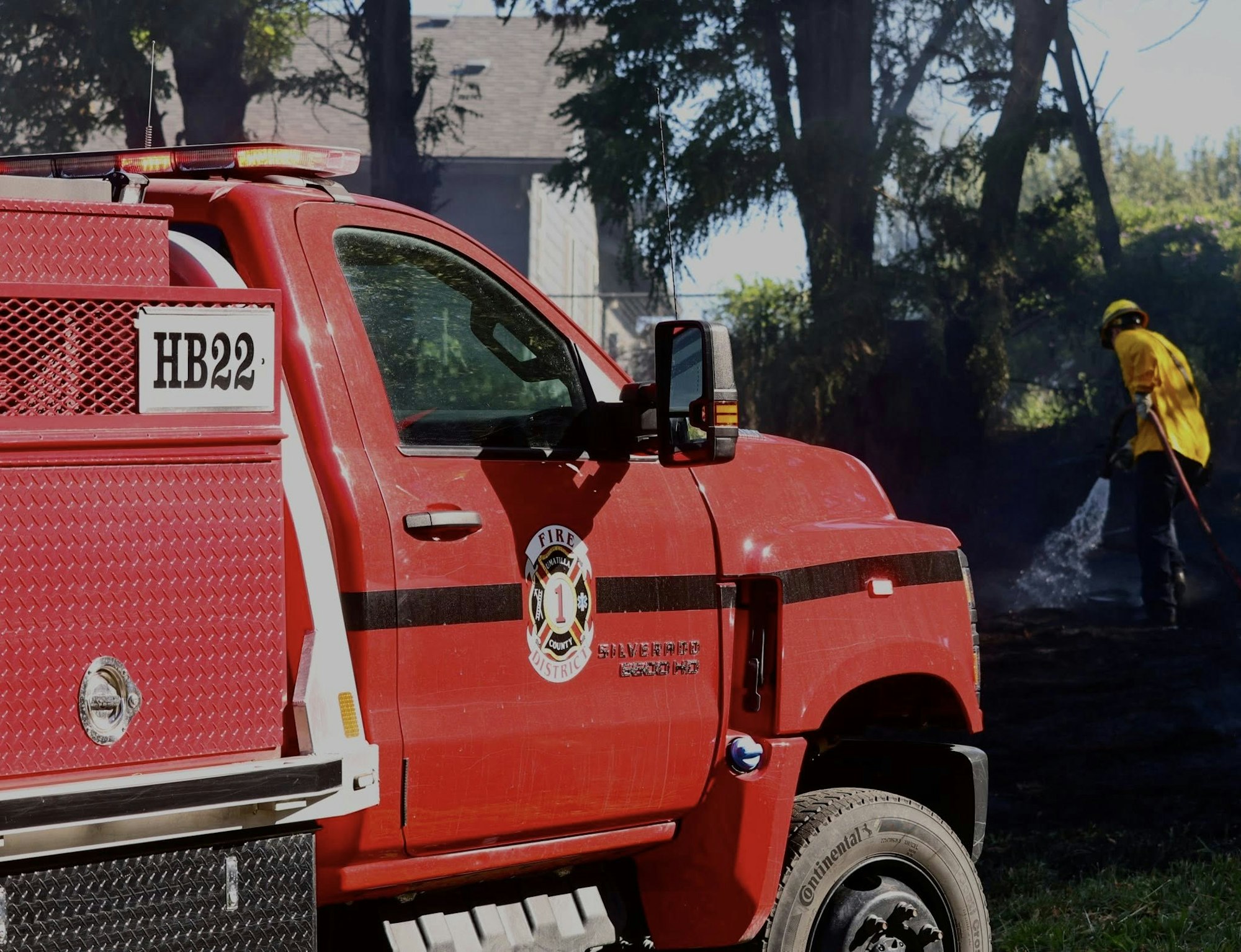 Red fire truck and firefighter spraying water in a wooded area.