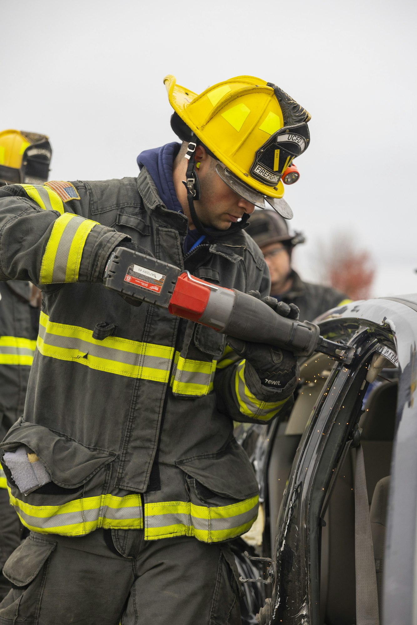 A firefighter is using a power tool on a car during a rescue operation.