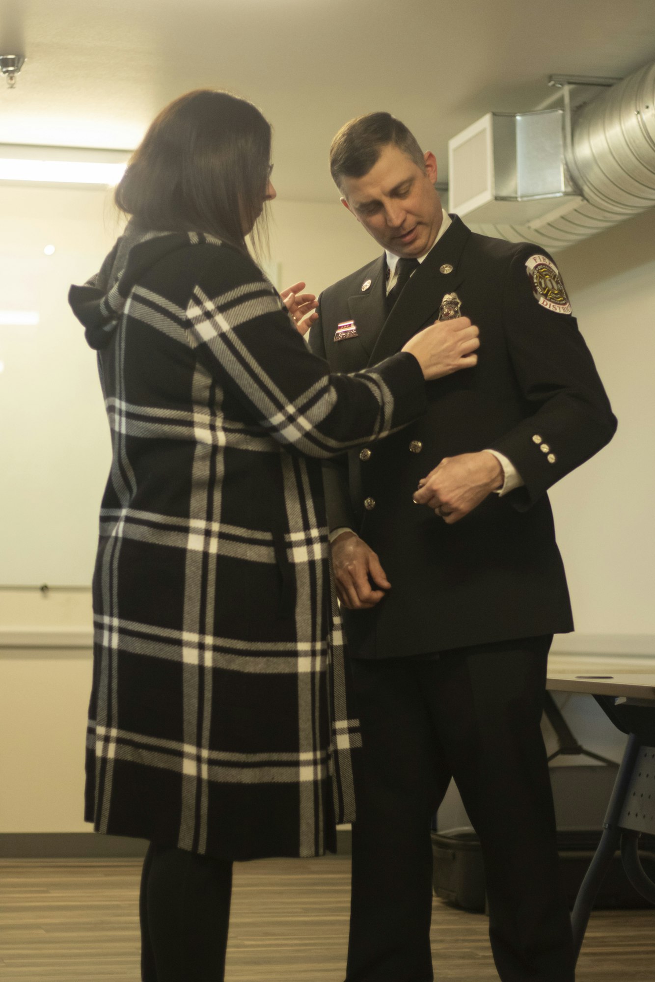 A person helps a man in a uniform with his badge in an indoor setting.