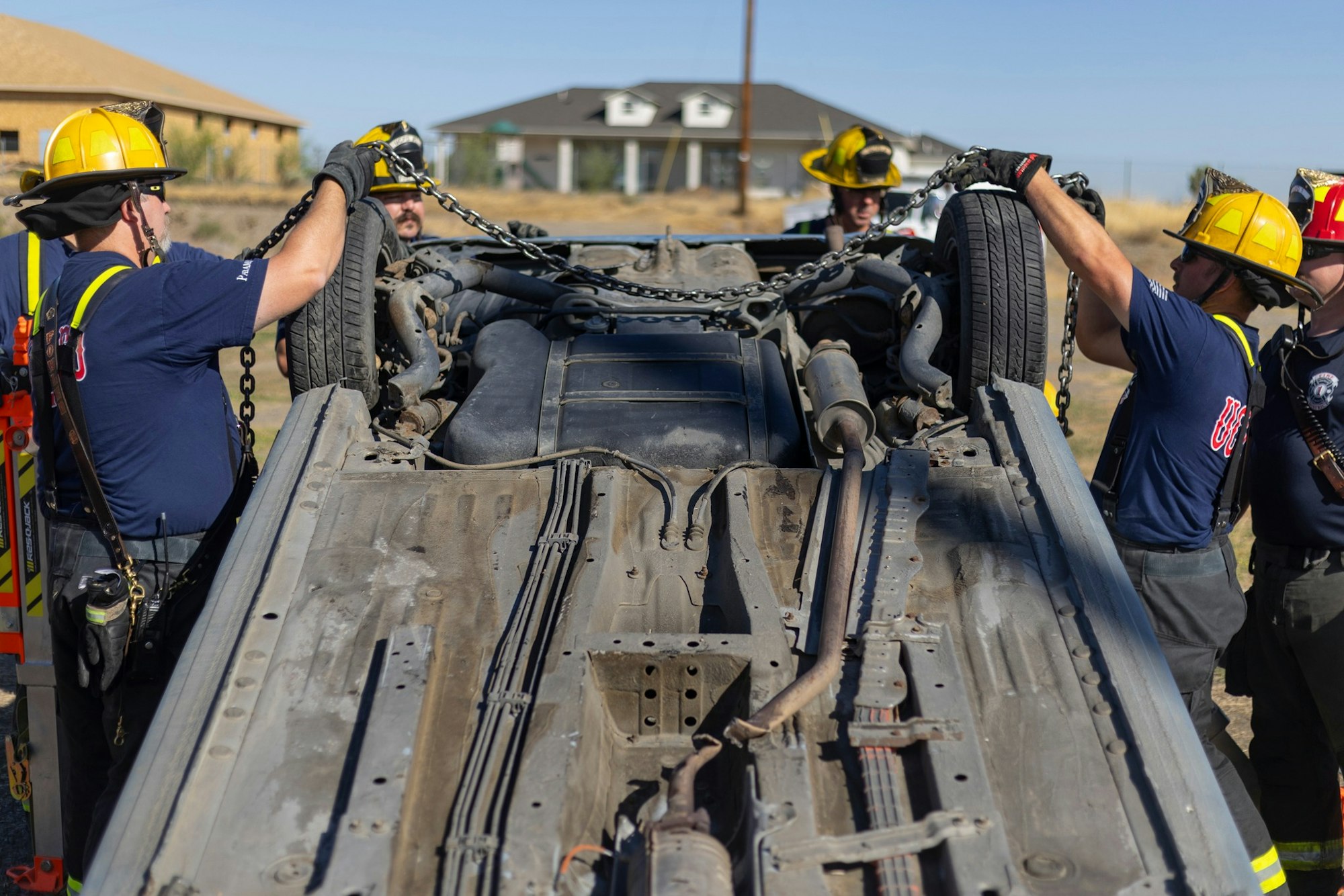 Firefighters in helmets and gloves use chains to stabilize an overturned vehicle.