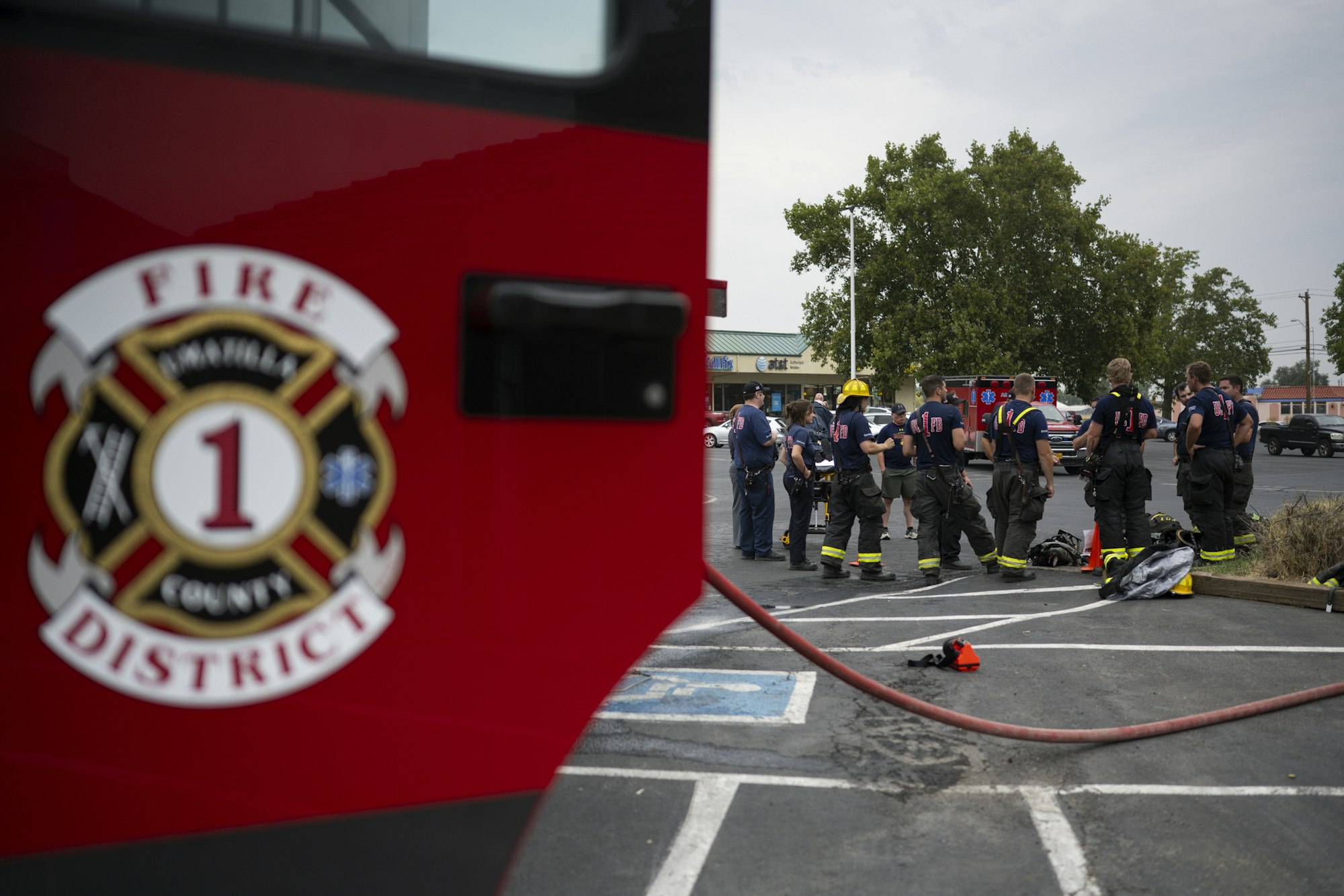 Firefighters gathered in a parking lot with fire truck and equipment, fire department emblem visible.