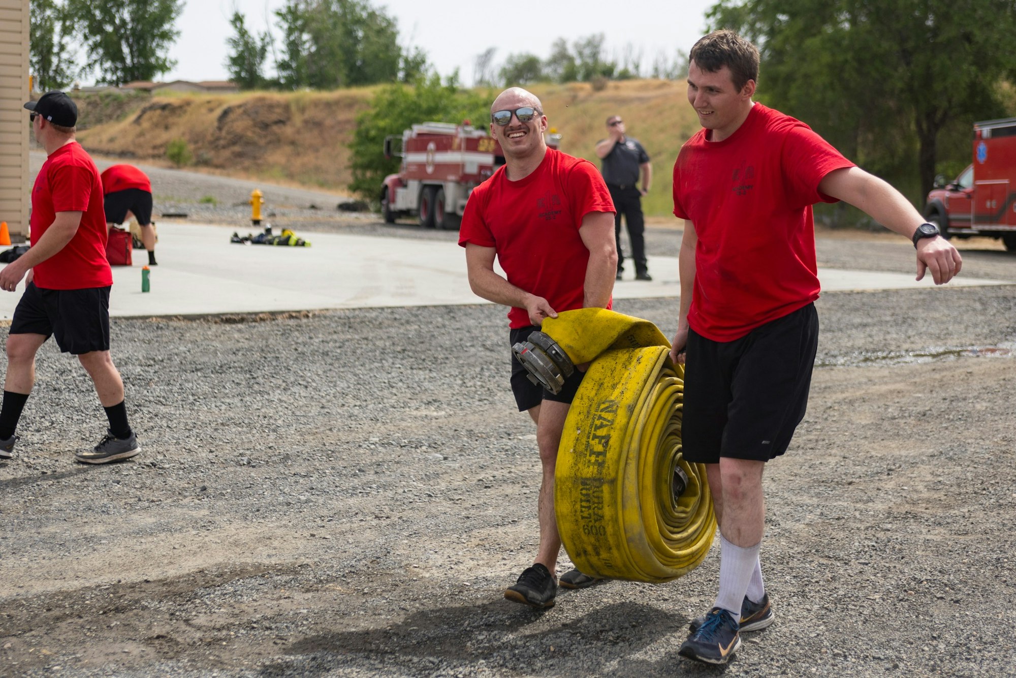Two people in red shirts carrying a large yellow fire hose outdoors.