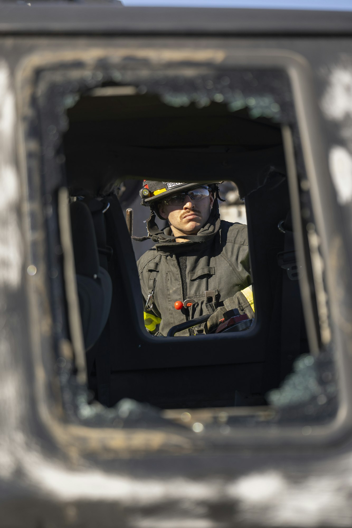 A firefighter in gear is visible through a shattered vehicle window, focused and ready for action.