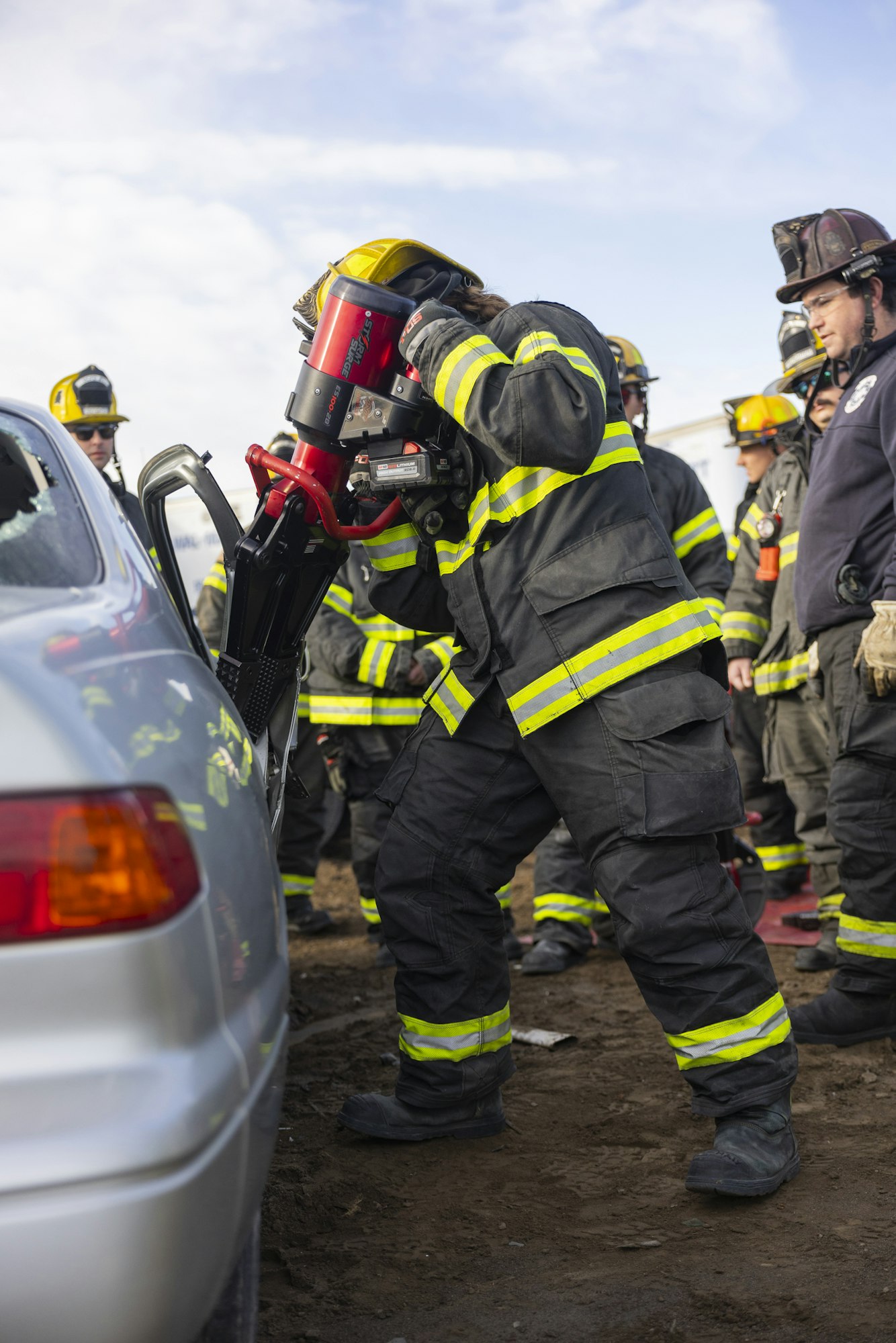 Firefighters using rescue tools on a car door, possibly during a training exercise or emergency scenario.