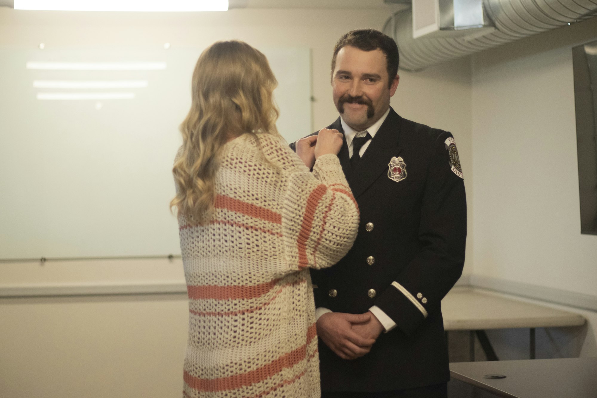 A person in a uniform receiving a pin from another person in a cozy room.