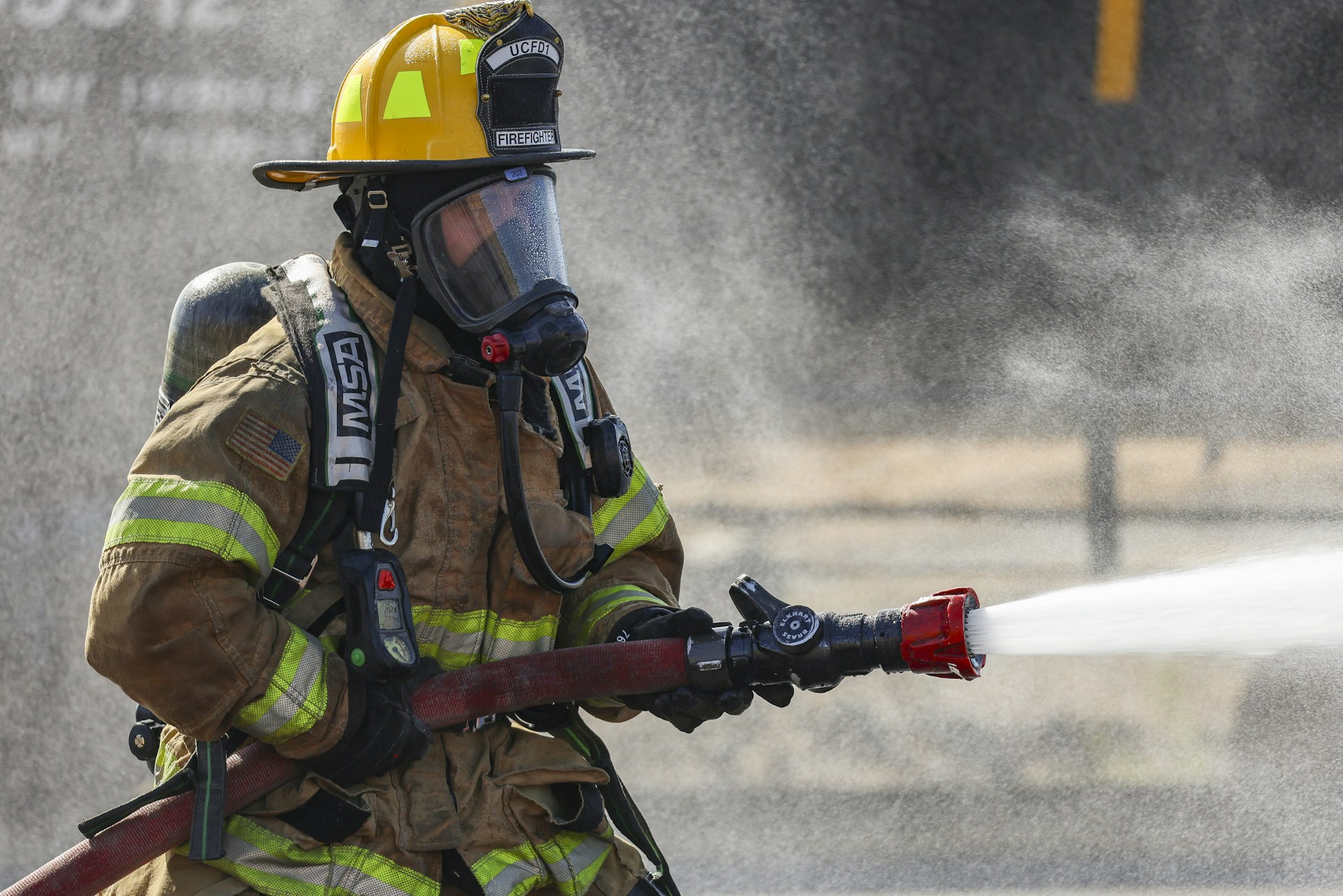 Firefighter in gear spraying water from a hose.