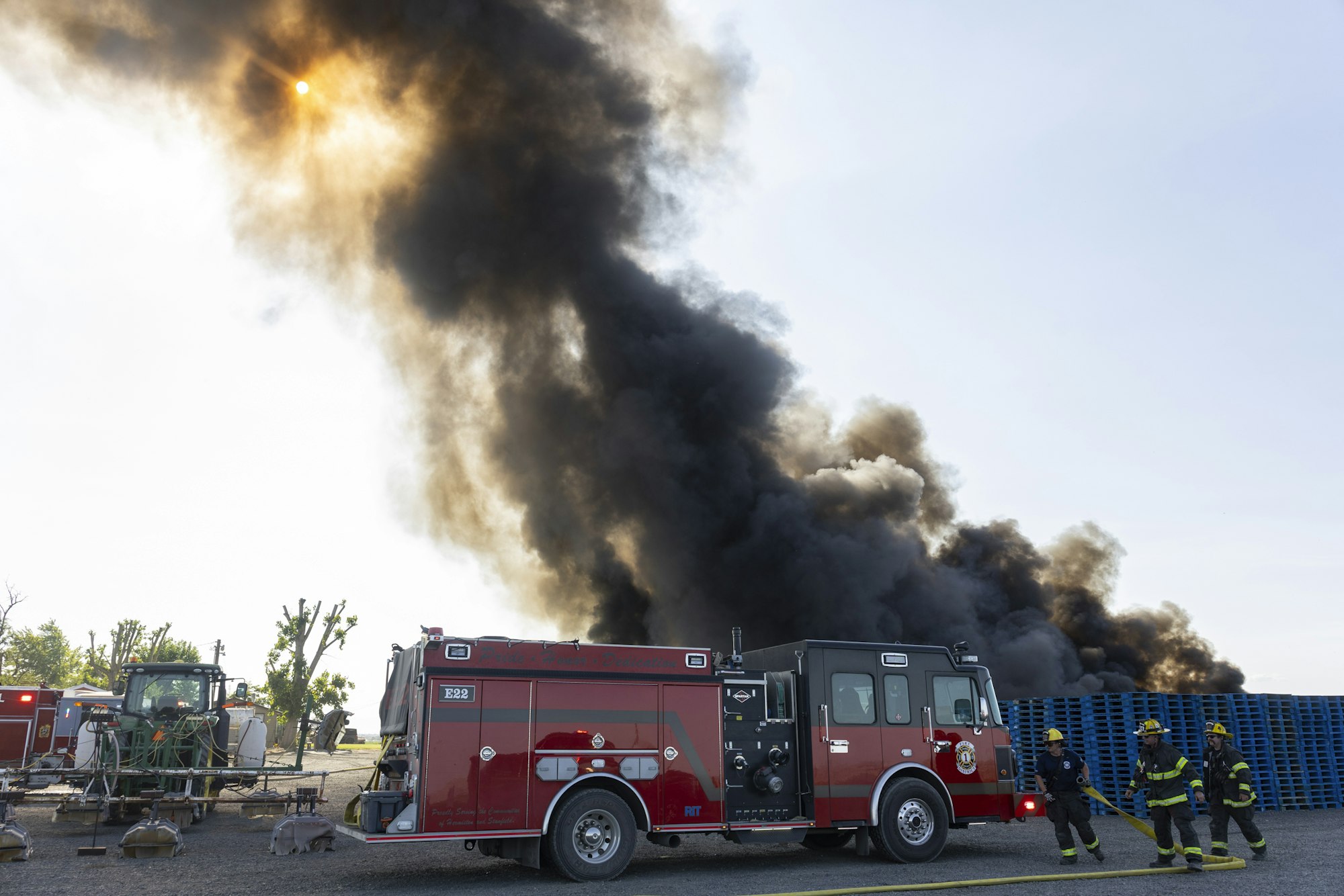 Firefighters and a fire truck at a scene with heavy black smoke billowing into the sky.