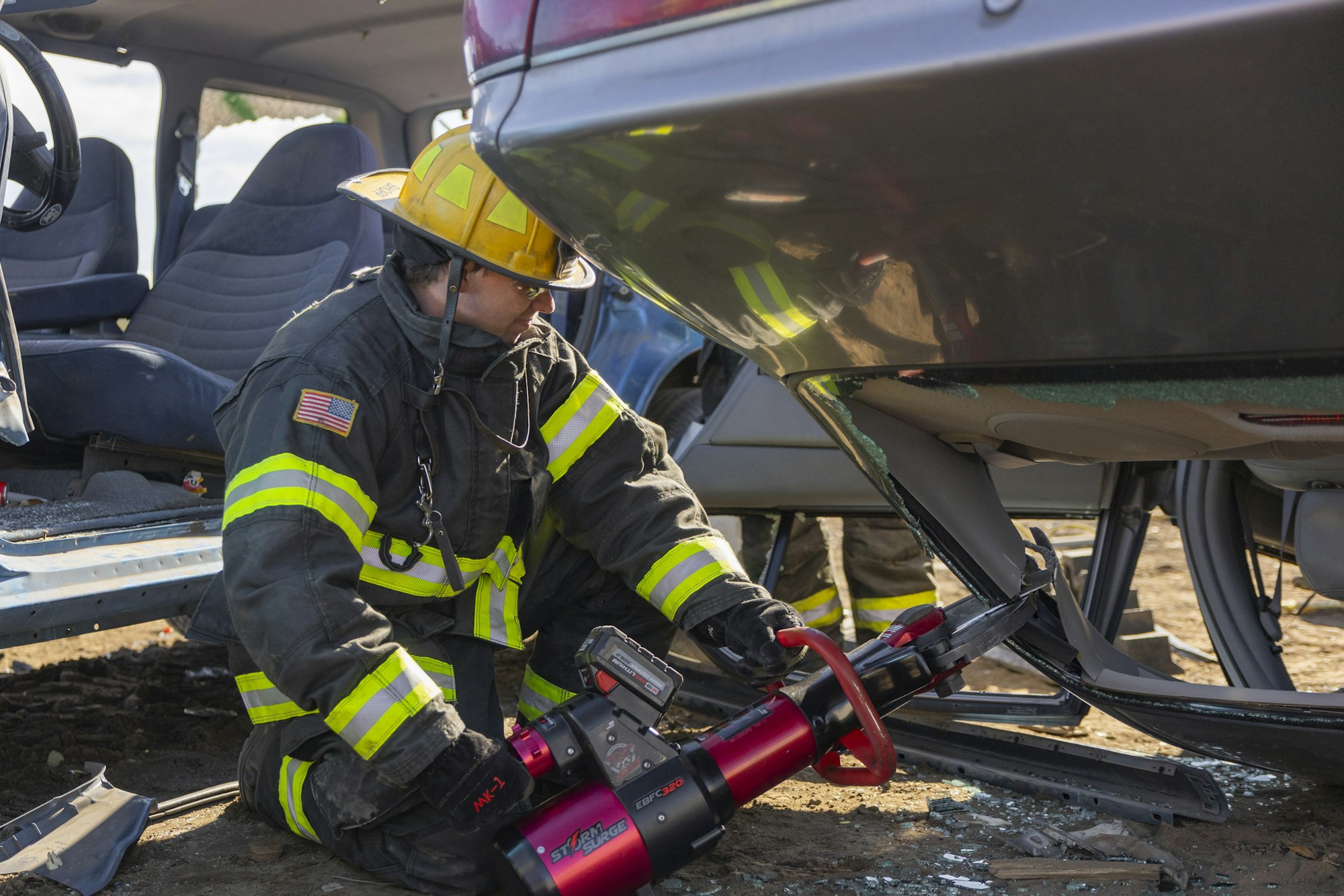Firefighter using hydraulic rescue tool on a car in a training exercise.