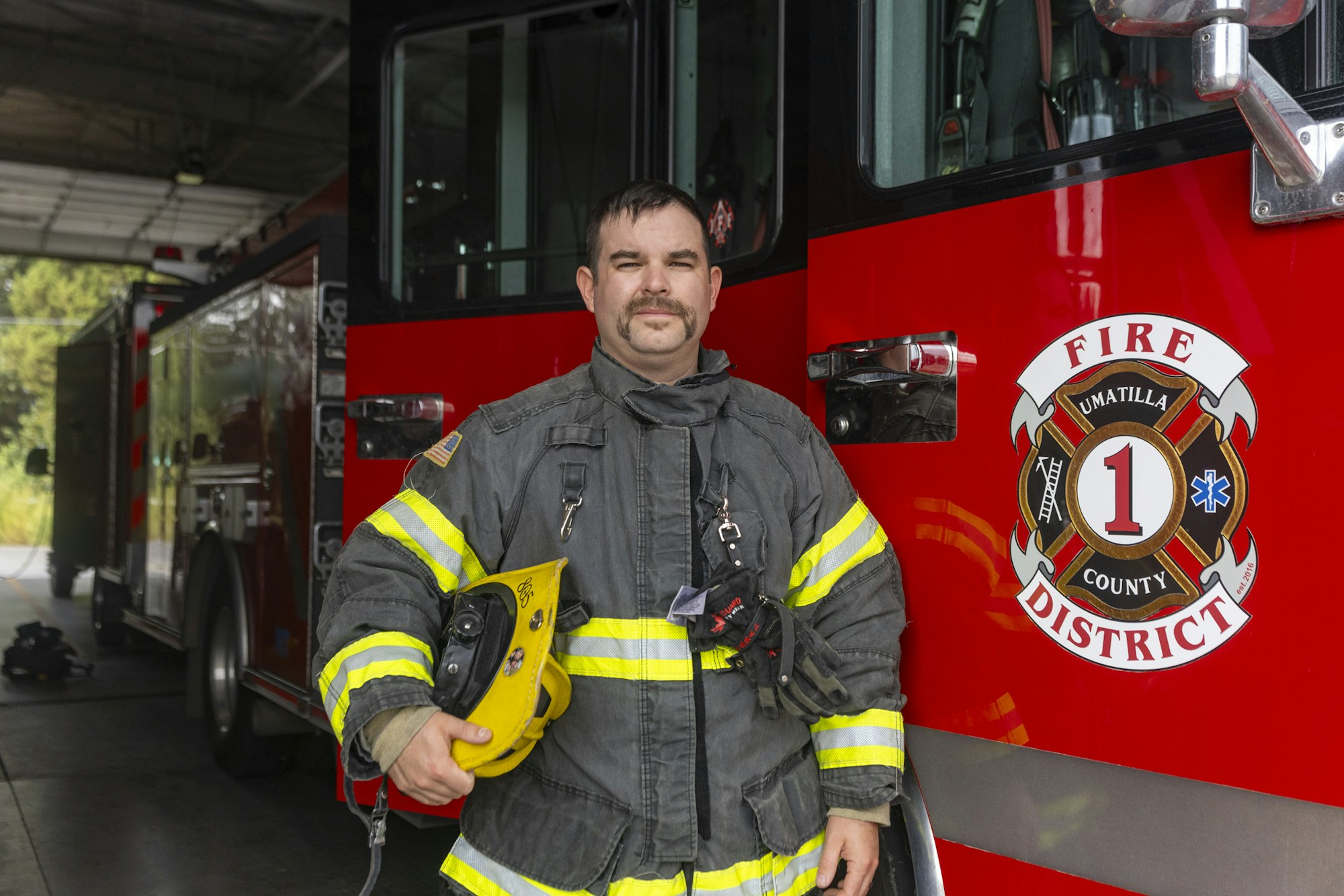 A firefighter in gear stands beside a fire truck labeled "Umatilla County Fire District 1."