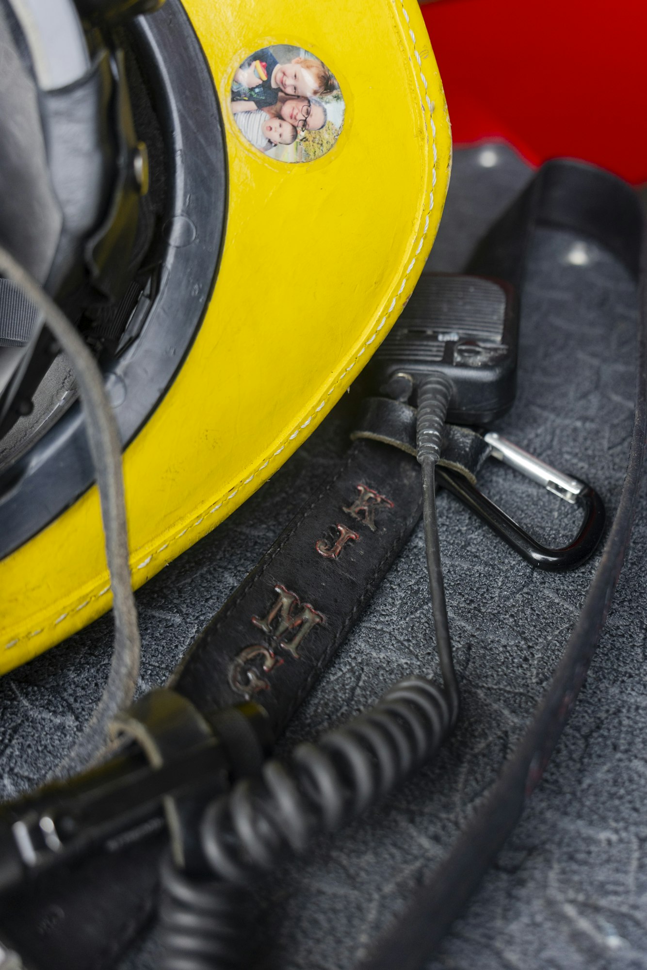 A yellow helmet with a family photo sticker, a cable, and a leather strap with "KJMG" initials.