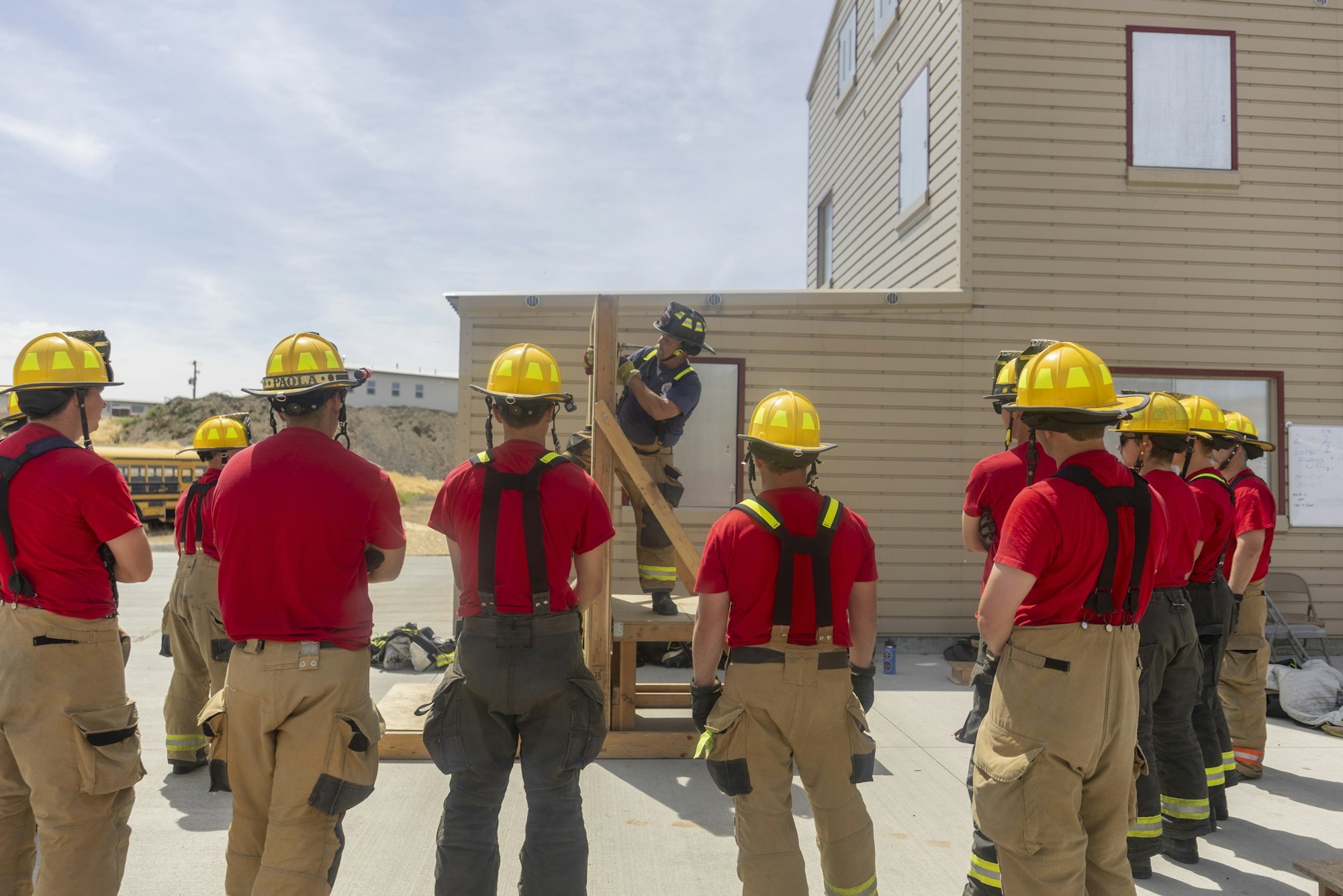 A group of firefighters in yellow helmets and red shirts receive training outdoors.