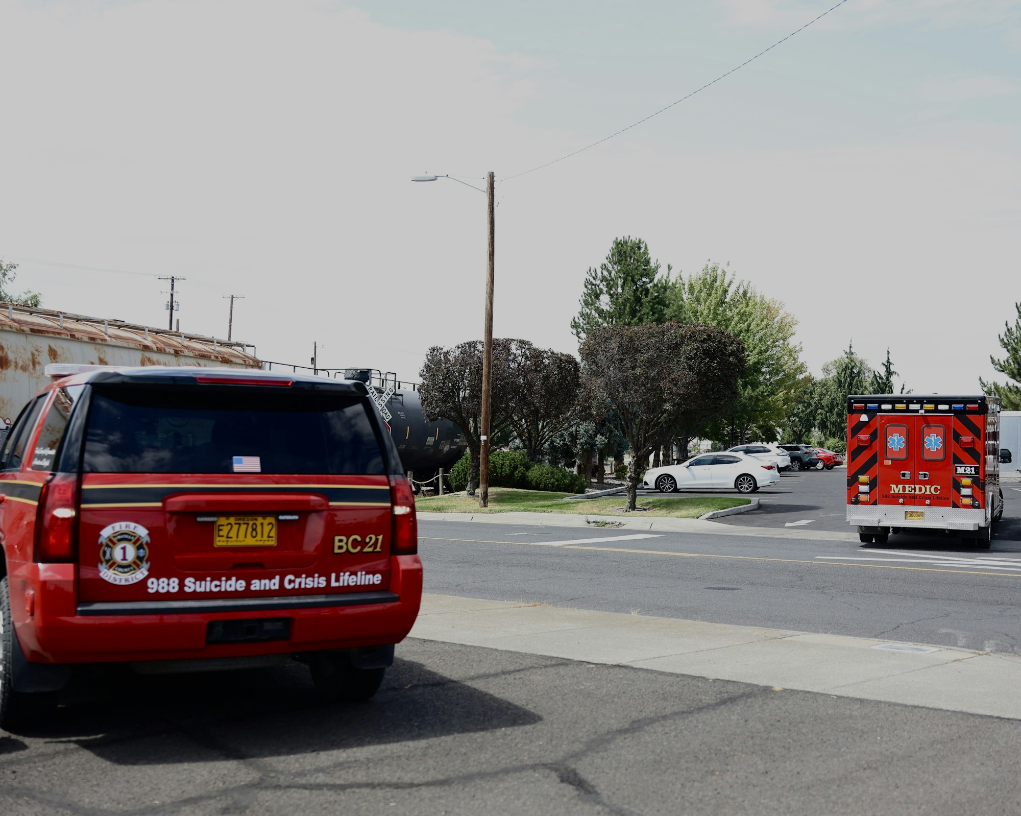 Red emergency response vehicle and ambulance near a parked white car, with a suicide and crisis lifeline number visible.
