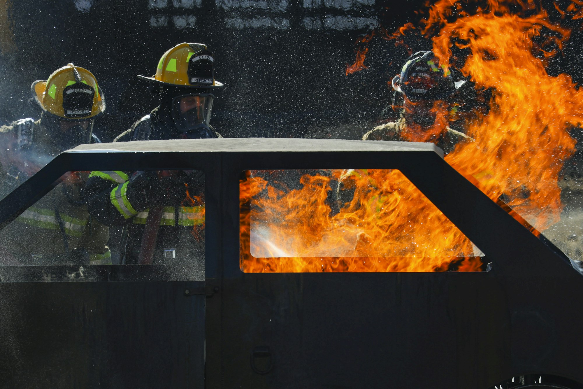 Firefighters extinguishing a blazing vehicle fire with heavy smoke and flames.