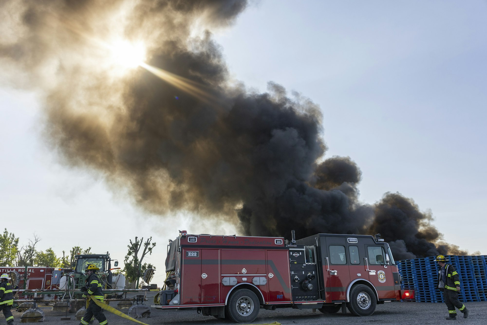 Firefighters and fire trucks with large smoke cloud in the background.