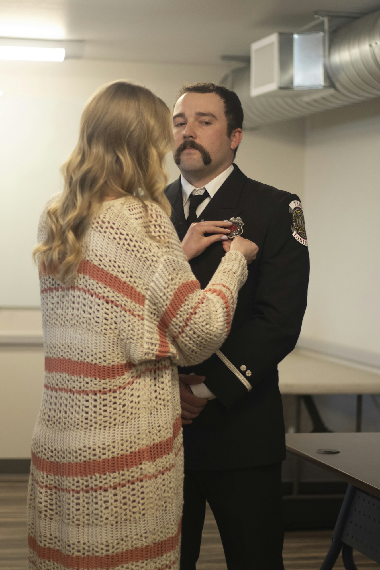 A woman pins a badge on a man in a formal uniform, possibly at a ceremony.