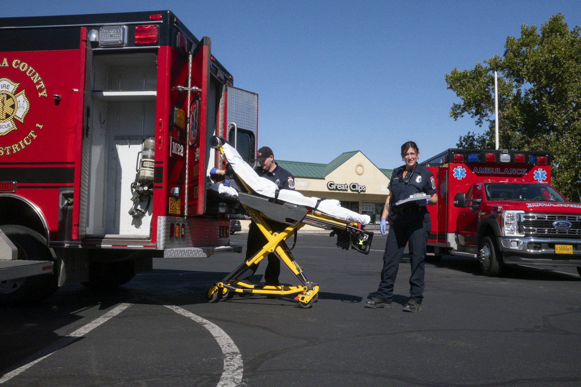 Two paramedics with a stretcher beside fire and ambulance vehicles in a parking lot.