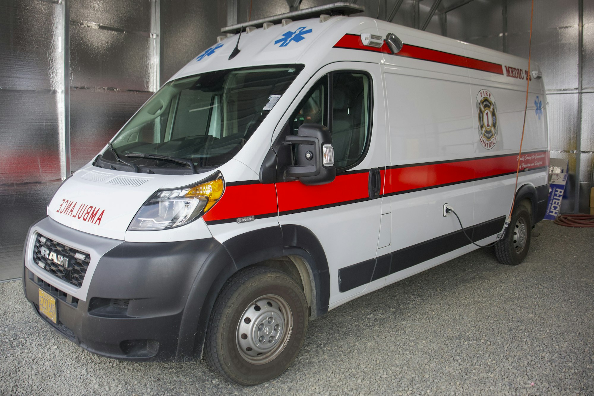 A white and red ambulance parked indoors with medical symbols and the word "AMBULANCE" on the front.